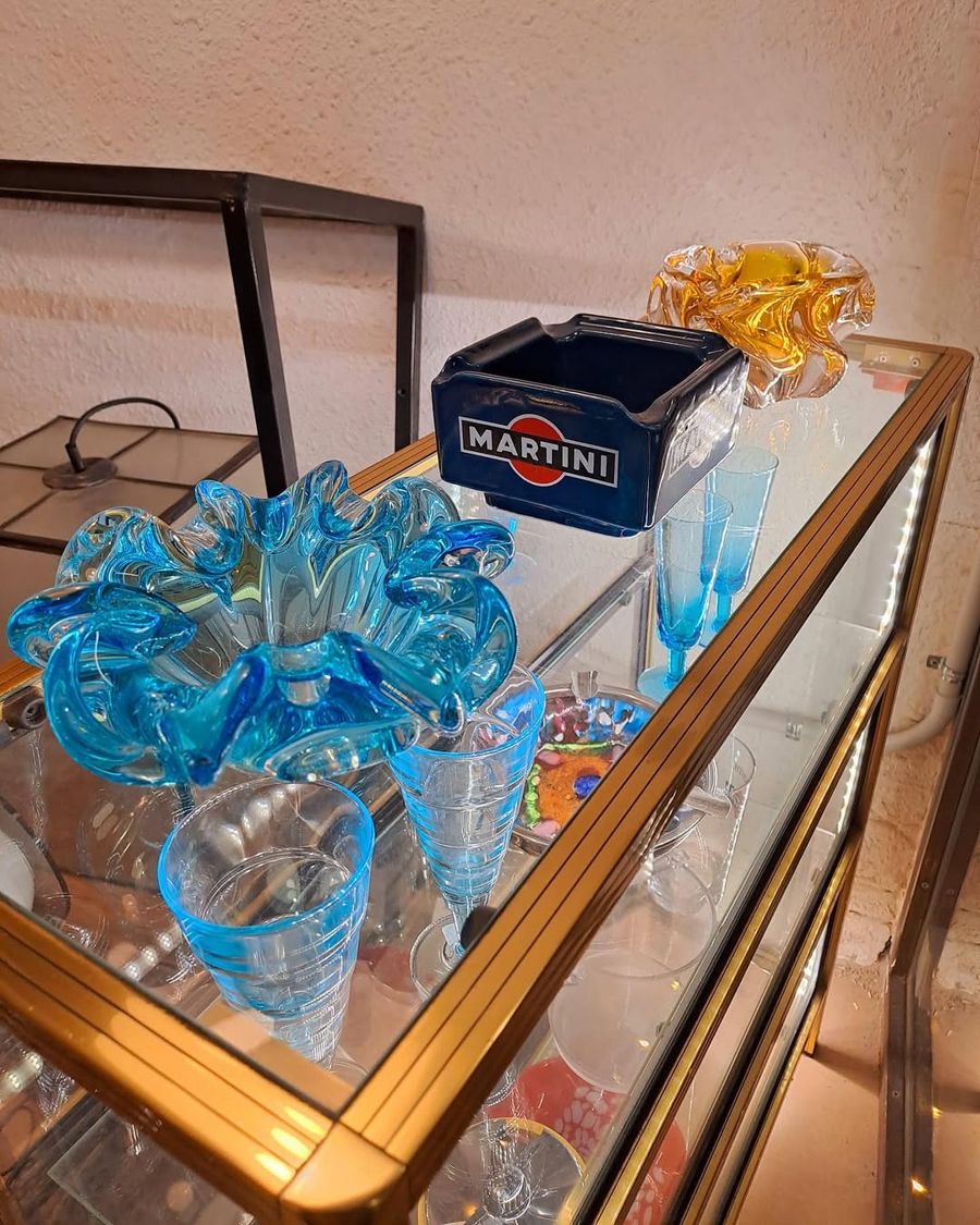 Centre de vidre blau, gots blaus i un cendrer de Martini sobre una vitrina daurada
